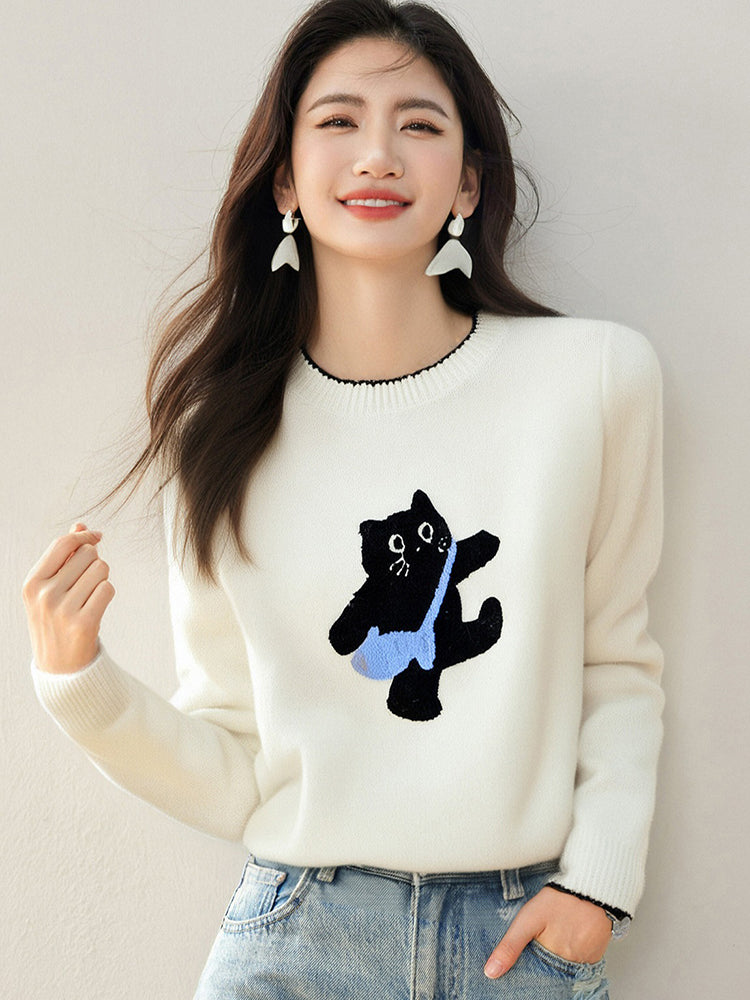 Woman wearing a white sweater with a black cat carrying a blue bag design against a plain background