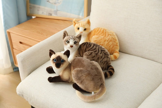 siamese cat, orange cat, and chartreux cat realistic stuffed cats on a couch