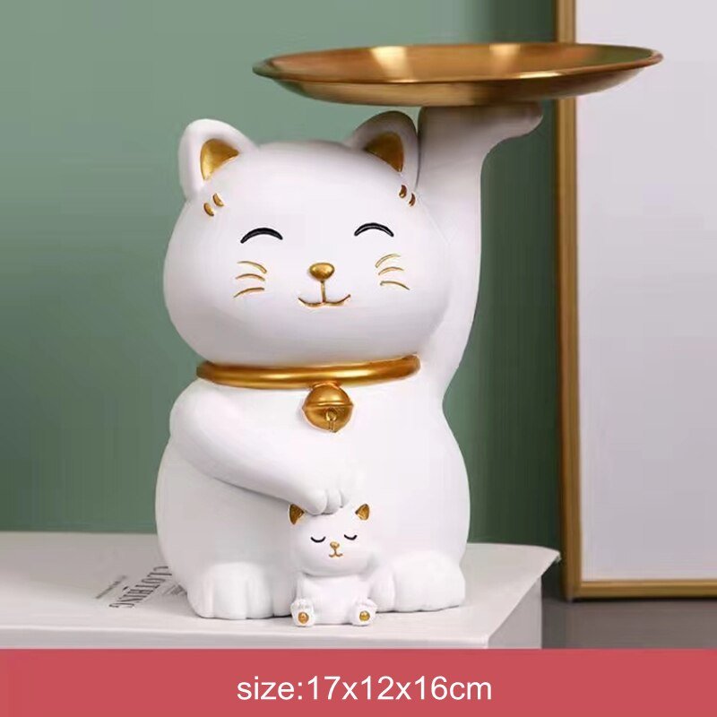 a white and gold color cat sculpture holding a tray and a baby