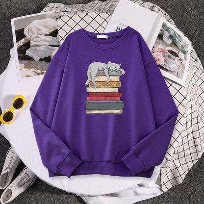 a purple sweatshirt with cat sleeping on a stack of books