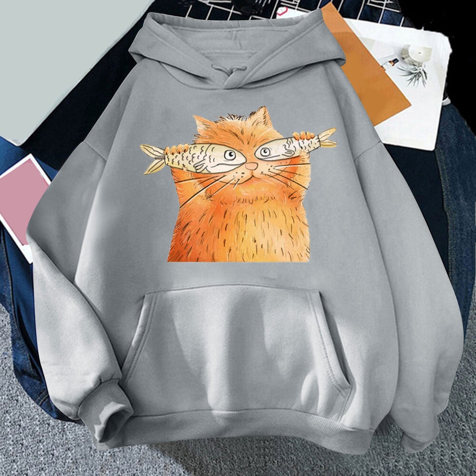 gray hoodie featuring a cartoon drawing  of a cat holding two fish and looking adorable