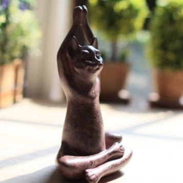 a cat figure in hands over head yoga pose in the garden